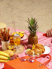 Picnic on the sandy beach. Fruit, drinks and beach accessories on a pink blanket.