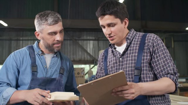 Medium shot of two men standing together in carpentry shop and discussing wooden detail