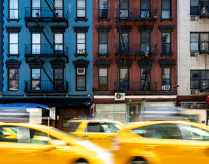 New York City street scene with yellow taxis driving past a block of old apartment buildings in the...
