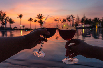 Cheerful couple drinking red wine in luxury resort at sunset