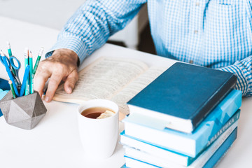 man in blue shirt reading book on modern stylish work place with office supplies and books, desk work concept in white and blue colors.