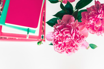 bouquet of pink peonies, a stack of books, pencils and a notebook on a white table, top view.