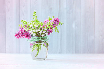 a small bouquet of lilacs and lilies of the valley in a vase. floral background with spring flowers. bouquet of delicate flowers close-up.