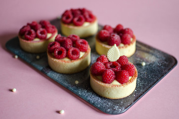 Mini tarts with fresh raspberry decorated with chocolate elements on pink background