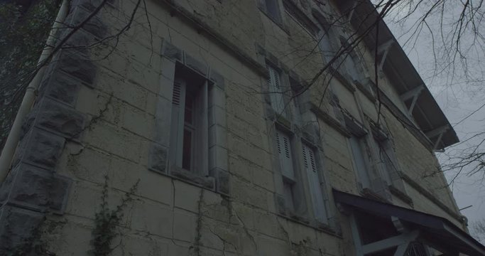 Abandoned house with Tree branches moving in the wind at night in a scary cloudy gray sky. Atmosphere horror, fear, creepy, Halloween Night in RED EPIC 6K. Plants growing on the walls. Static Shot.