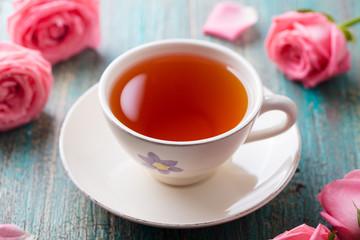 Cup of tea with pink rose. Colorful turquoise wooden background. Close up.