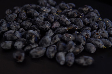 Ripe honeysuckle berries against black backdrop, place for text. Dark blue berry background. Concept of healthy and proper nutrition.