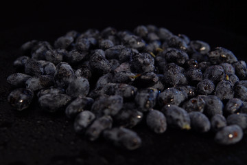 Ripe honeysuckle berries with droplets of water on against black backdrop, place for text. Dark blue berry background.Concept of healthy and proper nutrition.
