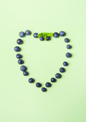 Fresh blueberries in shape of heart frame on pastel green background. Healthy breakfast concept