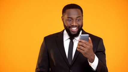 Joyful african businessman holding smartphone and smiling, online booking app