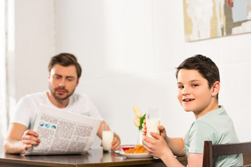 father with newspaper and smiling son having breakfast together