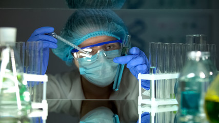 Laboratory worker mixing green and blue liquids, checking experiment results