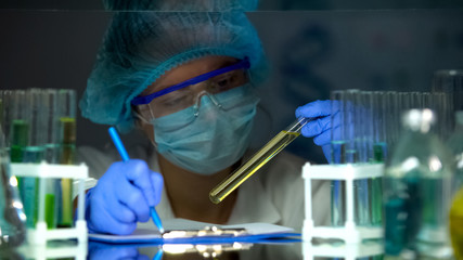Medical lab worker checking urine sample in tube, writing results, doping test