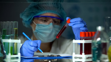 Doctor checking tube with blood analysis and making notes, lymphoma cancer