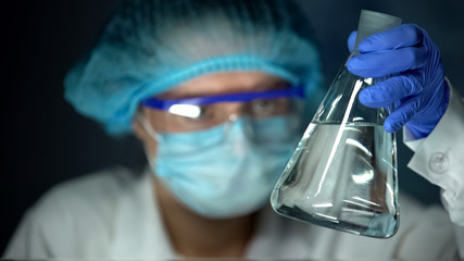 Lab assistant holding flask with transparent liquid, spirit production, vodka