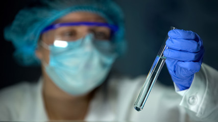 Lab worker holding water sample in test tube, analyzing minerals concentration