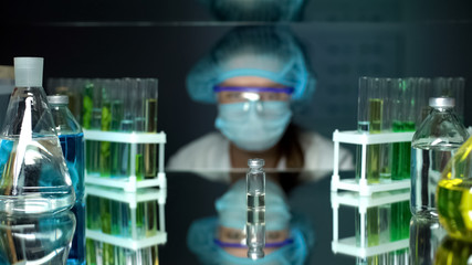 Laboratory assistant looking at bottle with transparent liquid, vaccine analysis