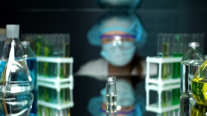 Bottle with transparent liquid on table in front of lab worker, researches