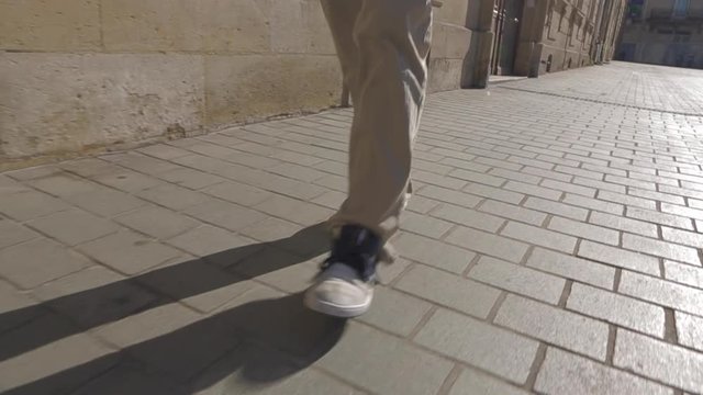 Close up shot of skater skateboarder man legs walking on cobblestone street, wearing brown jean and grey urban shoes, slow motion during summer afternoon in France.