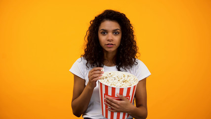 Beautiful African-American woman eating popcorn isolated on yellow background