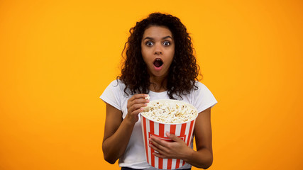 Excited African-American woman eating popcorn and watching interesting movie