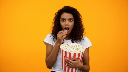 Focused African-American woman eating popcorn and watching interesting show