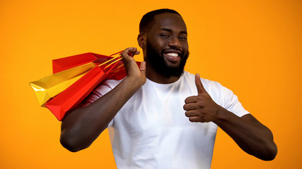 Black man holding shopping bags and showing thumbs up sign, season discount