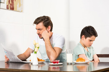 father reading newspaper and offended son during breakfast