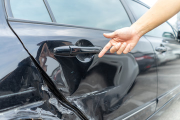 Man hand pointing on car bumper dented broken on black car door.