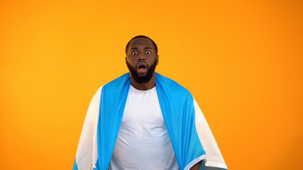 Shocked African-American man watching sport match, Argentina flag on shoulders