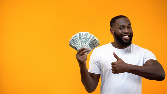 Afro-American man holding bunch of dollars and showing thumbs up, start-up
