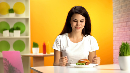 Obraz na płótnie Canvas Beautiful female looking at tasty burger, breakfast in fast food restaurant