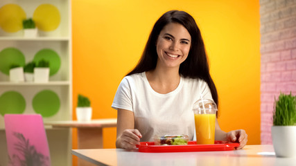 Obraz na płótnie Canvas Happy woman smiling, tray with salad and fresh orange juice on table, snack bar