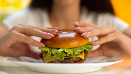 Female hands taking tasty cheeseburger from white plate closeup, cholesterol