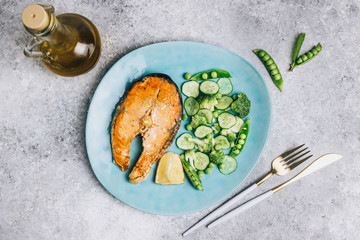 Salmon steak and green salad with cucumber, broccoli and peas.