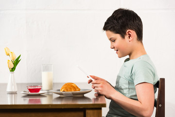 side view of smiling boy using digital tablet during breakfast in kitchen