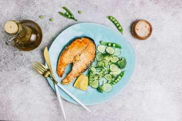 Salmon steak and green salad with cucumber, broccoli and peas.