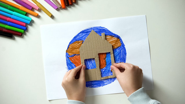 Kid putting paper house near Earth painting, world our home, saving planet
