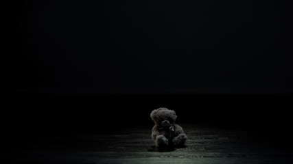 Teddy bear toy in dark room, loneliness and lost childhood concept, sadness