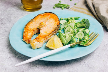 Salmon steak and green salad with cucumber, broccoli and peas.