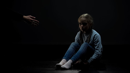 Female kid in dark room looking at adult helping hand, social security concept