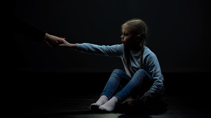 Little child in dark room accepting adult helping hand, social security concept