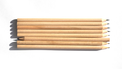 Many pencils are on the table in bright daylight. Natural unpainted wood. Eco-friendly materials. Not like everyone else