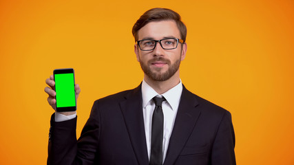 Serious man in suit holding green screen smartphone, online schedule app