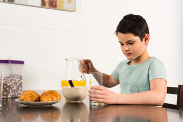 Fototapeta na wymiar boy holding glass and jug with orange juice in kitchen