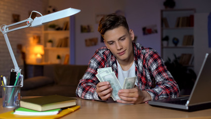 Fototapeta na wymiar Teenager counting dollars sitting on desk, planning new purchase, dreaming