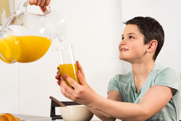 cropped view of father pouring orange juice to son in kitchen