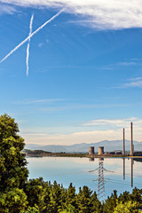 View of X shaped chemtrails above coal power plant by the lake.