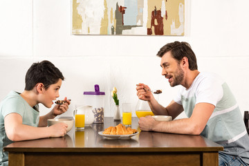 smiling father and son having breakfast and looking at each other in kitchen