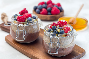Layered chocolate and peanut butter chia seed pudding in jar, garnished with raspberry, blueberry, honey and coconut flakes, horizontal